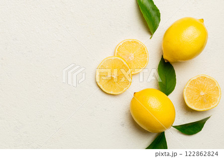 Many fresh ripe lemons with green leaves on colored background, top view, space for text 122862824
