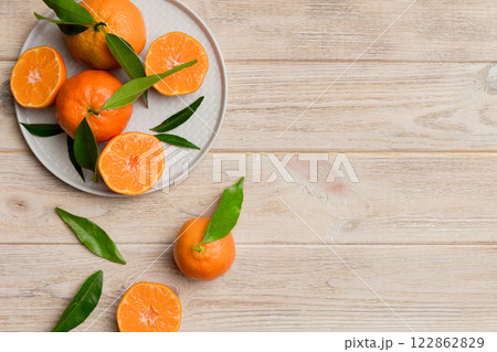 Fresh cutted clementines and whole mandarin over round plate on colored background. Food and drink ingredients preparing. healthy eating theme top view vith copy space 122862829