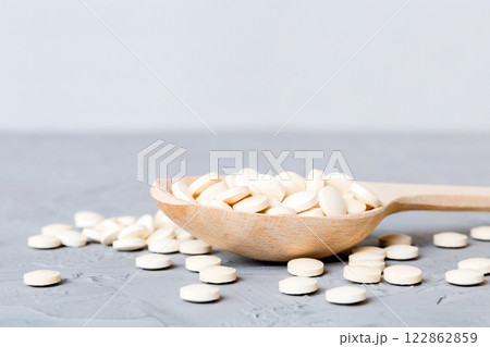 Heap of white pills on colored background. Tablets scattered on a table. Pile of red soft gelatin capsule. Vitamins and dietary supplements concept Heap of white pills on colored background. Tablets scattered on a table. Pile of red soft gelatin capsule. Vitamins and dietary supplements concept 122862859
