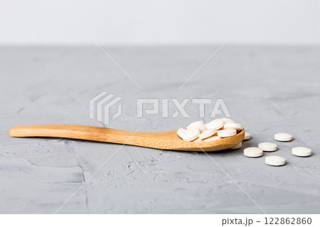 Heap of white pills on colored background. Tablets scattered on a table. Pile of red soft gelatin capsule. Vitamins and dietary supplements concept 122862860