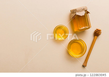 Glass jar of honey with wooden drizzler on colored background. Honey pot and dipper high above. Top view copy space Glass jar of honey with wooden drizzler on colored background. Honey pot and dipper high above. Top view copy space 122863045
