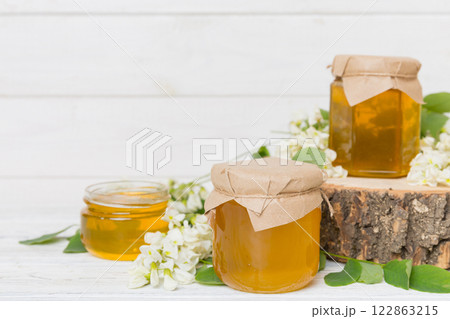 Sweet honey jar surrounded spring acacia blossoms. Honey flows from a spoon in a jar. jars of clear fresh acacia honey on wooden background 122863215