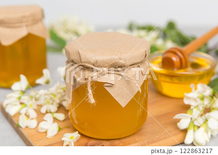 Sweet honey jar surrounded spring acacia blossoms. Honey flows from a spoon in a jar. jars of clear fresh acacia honey on wooden background Sweet honey jar surrounded spring acacia blossoms. Honey flows from a spoon in a jar. jars of clear fresh acacia honey on wooden background 122863217