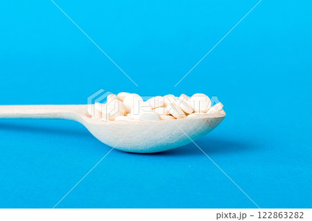 Heap of white pills on colored background. Tablets scattered on a table. Pile of red soft gelatin capsule. Vitamins and dietary supplements concept Heap of white pills on colored background. Tablets scattered on a table. Pile of red soft gelatin capsule. Vitamins and dietary supplements concept 122863282