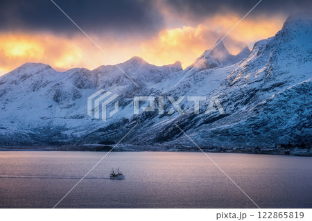 Snowy mountains in clouds, bright sunbeams, boat in fjord 122865819