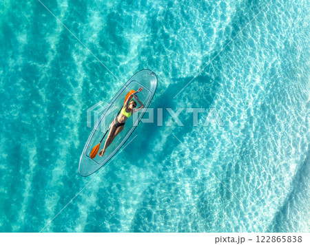 Aerial view of young woman lying on transparent canoe in blue se 122865838