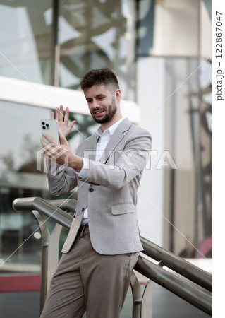 Walking young businessman commuting, having fun doing video call using mobile phone walking to work during his morning commute in the city. 122867047