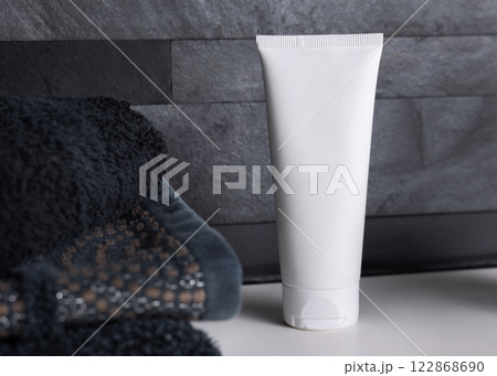 White cream tube near black folded towels on basin in dark grey bathroom close up, cosmetic mockup White cream tube near black folded towels on basin in dark grey bathroom close up, cosmetic mockup 122868690