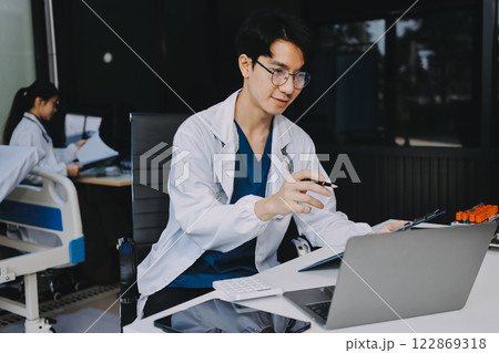 Positive doctor working on laptop in medical office, portrait. 122869318