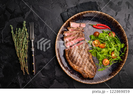 Grilled striploin steak, beef meat steak on a plate with salad. black background. top view 122869859