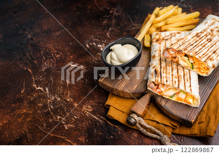 Shawarma chicken roll with fresh vegetables, cream sauce and french fries on wooden board. brown background. top view 122869867