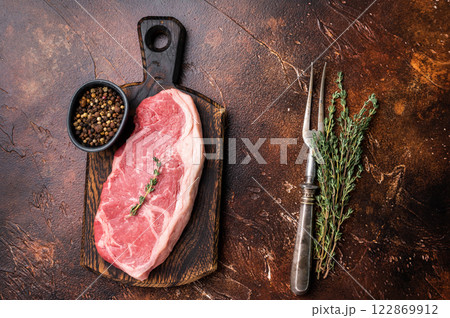 Raw New York strip beef steak, also named Striploin steak on a wooden board. brown background. top view 122869912