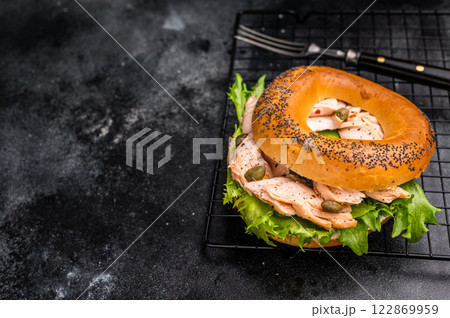 Bagel sandwich with lox, smoked salmon, lettuce and cream cheese on a rack. black background. top view Bagel sandwich with lox, smoked salmon, lettuce and cream cheese on a rack. black background. top view 122869959