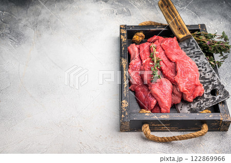 Raw horse meat slices in a wooden tray, showcasing its appealing color and texture, ready for cooking. grey background. top view Raw horse meat slices in a wooden tray, showcasing its appealing color and texture, ready for cooking. grey background. top view 122869966