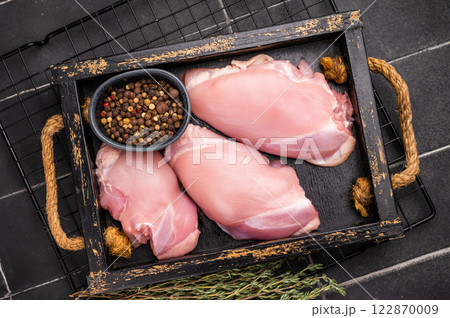 Raw Chicken thighs fillets in a wooden tray. black background. top view 122870009