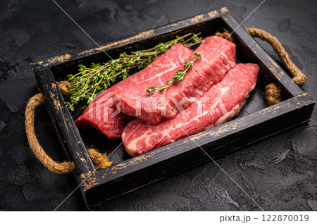 Raw skirt or machete Steak, beef meat in wooden tray with herbs. black background. top view Raw skirt or machete Steak, beef meat in wooden tray with herbs. black background. top view 122870019
