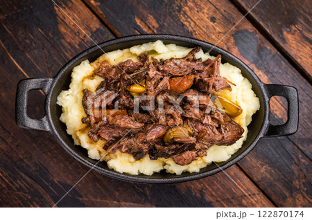 Braised Beef Cheek, Slow cooked meat with smashed potatoes in a skillet. wooden background. top view Braised Beef Cheek, Slow cooked meat with smashed potatoes in a skillet. wooden background. top view 122870174