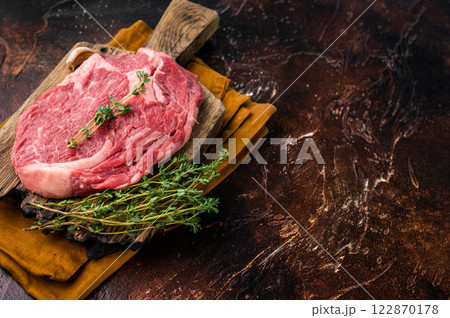 Fresh Marbled Rib eye steak with herbs on butcher cutting board, raw beef meat. brown background. top view Fresh Marbled Rib eye steak with herbs on butcher cutting board, raw beef meat. brown background. top view 122870178