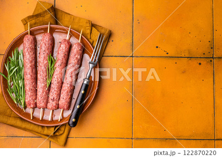 Raw Turkish Urfa kebab skewers on a plate with herbs. orange background. top view 122870220
