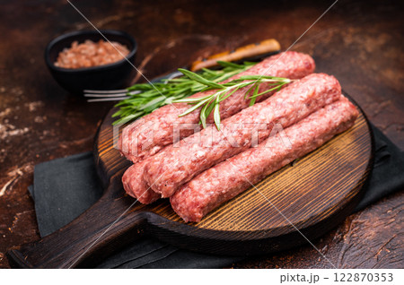 Fresh raw beef and lamb meat kebabs sausages on wooden board. brown background. top view Fresh raw beef and lamb meat kebabs sausages on wooden board. brown background. top view 122870353