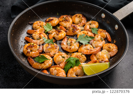 Fried Shrimps Prawns with garlic and butter in a skillet. Black background. Top view Fried Shrimps Prawns with garlic and butter in a skillet. Black background. Top view 122870376