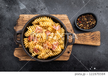 Fusilli carbonara pasta topped with crispy bacon bits and parmesan cheese in a skillet. Black background. Top view Fusilli carbonara pasta topped with crispy bacon bits and parmesan cheese in a skillet. Black background. Top view 122870384