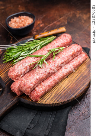 Fresh raw beef and lamb meat kebabs sausages on wooden board. brown background. top view Fresh raw beef and lamb meat kebabs sausages on wooden board. brown background. top view 122870385