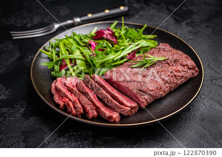 Grilled and sliced Flank beef steak on plate with salad. black background. top view 122870390