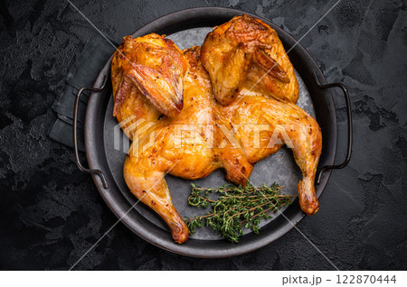Roasted chicken Tabaka with herbs and spices, poultry meat on steel tray. black background. top view Roasted chicken Tabaka with herbs and spices, poultry meat on steel tray. black background. top view 122870444