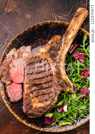 Grilled and sliced Tomahawk beef steak, marble rib eye with bone on plate with salad. brown background. top view Grilled and sliced Tomahawk beef steak, marble rib eye with bone on plate with salad. brown background. top view 122870471