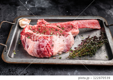 Ready for cooking Tomahawk beef steak with seasonings, raw marbled rib eye with bone on steel tray. black background. top view Ready for cooking Tomahawk beef steak with seasonings, raw marbled rib eye with bone on steel tray. black background. top view 122870539
