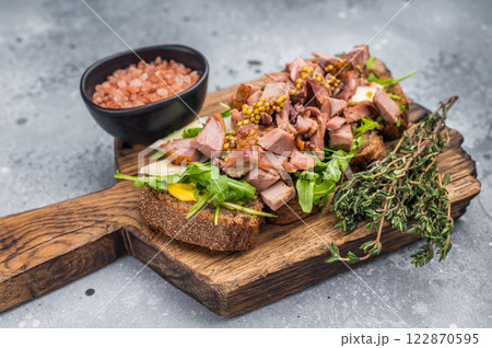 Open sandwich with duck fillet meat, foie gra liver, arugula and cheese on board. grey background. top view Open sandwich with duck fillet meat, foie gra liver, arugula and cheese on board. grey background. top view 122870595