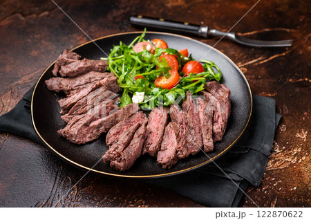 Grilled and sliced Beef Denver strip Steak on a plate with salad. brown background. top view 122870622