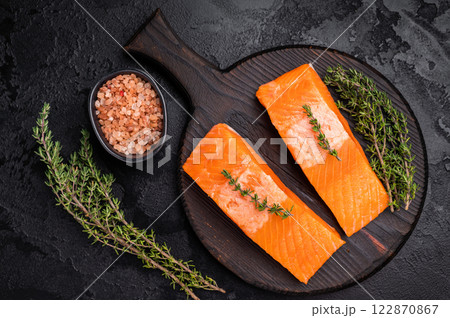 Fresh Salmon fillet steak, raw fish meat on a wooden board with herbs. black background. top view Fresh Salmon fillet steak, raw fish meat on a wooden board with herbs. black background. top view 122870867