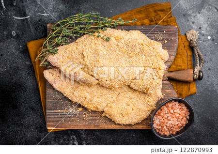 Wiener breaded raw pork Schnitzel, meat steak on a wooden board. black background. top view Wiener breaded raw pork Schnitzel, meat steak on a wooden board. black background. top view 122870993