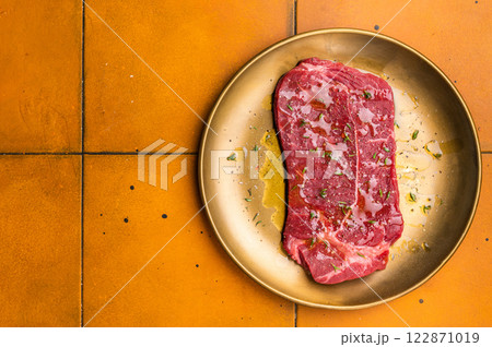 Marinated with olive oil and herbs Raw top sirloin or rump beef steak. orange background. top view 122871019