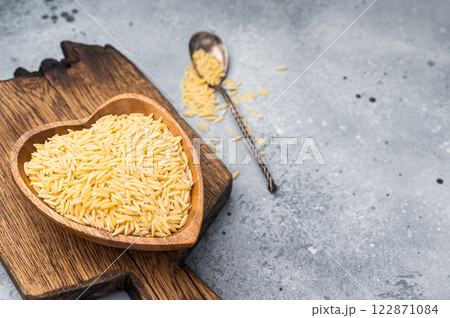Raw Orzo pasta, uncooked dry Italian risoni in a bowl. grey background. top view Raw Orzo pasta, uncooked dry Italian risoni in a bowl. grey background. top view 122871084