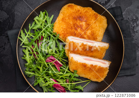 Chicken cordon bleu cutlet with cheese and ham on plate with salad. black background. top view 122871086
