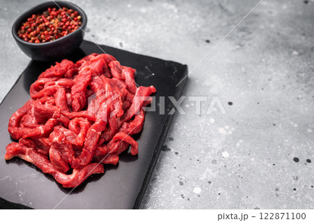 Pieces of Raw beef sliced meat, strips for cooking beef stroganov on board. grey background. top view 122871100