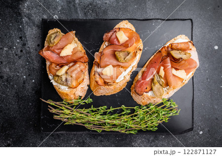 Prosciutto and pesto bruschetta, parmesan cheese and olives. black background. top view Prosciutto and pesto bruschetta, parmesan cheese and olives. black background. top view 122871127