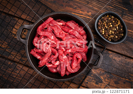 Raw beef meat sliced strips for beef stroganoff in a skillet. wooden background. top view Raw beef meat sliced strips for beef stroganoff in a skillet. wooden background. top view 122871171