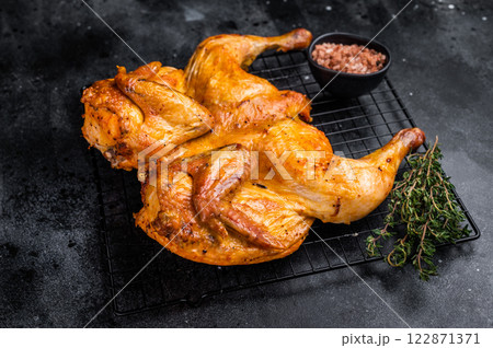 Roasted Spatchcock chicken with herbs and spices, poultry meat on steel rack. black background. top view 122871371