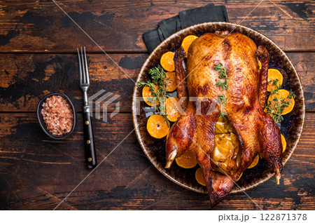 Roast goose with apples and oranges on plate with herbs. wooden background. top view 122871378