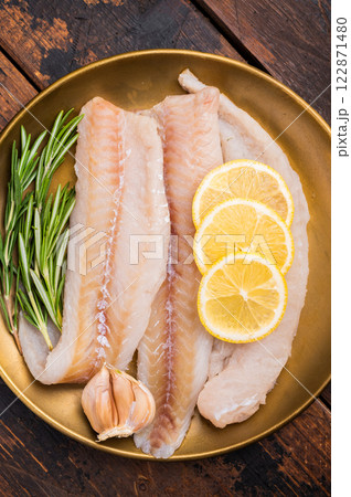 Pollock sea fish fillets, raw whitefish on a plate with herbs and lemon. wooden background. top view Pollock sea fish fillets, raw whitefish on a plate with herbs and lemon. wooden background. top view 122871480