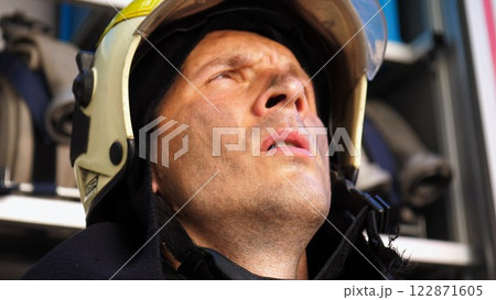 Young tired fireman in protective uniform against the background of a fire engine. Portrait of male firefighter with dirty face near fire truck. Concept of saving lives and heroic profession. Close up Young tired fireman in protective uniform against the background of a fire engine. Portrait of male firefighter with dirty face near fire truck. Concept of saving lives and heroic profession. Close up 122871605