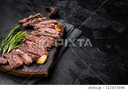 Roast Skirt Machete Steak, grilled beef meat on cutting board. black background. top view 122871696