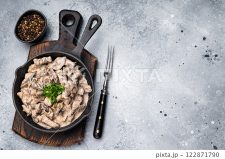 Creamy beef stroganoff with fresh greenery, savory mushroom sauce and caramelized onions in a skillet. grey background. top view Creamy beef stroganoff with fresh greenery, savory mushroom sauce and caramelized onions in a skillet. grey background. top view 122871790