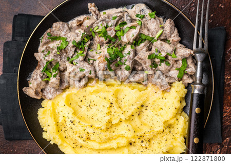Beef stroganoff with mashed potatoes, fresh greenery and savory mushroom sauce in a plate . brown background. top view 122871800