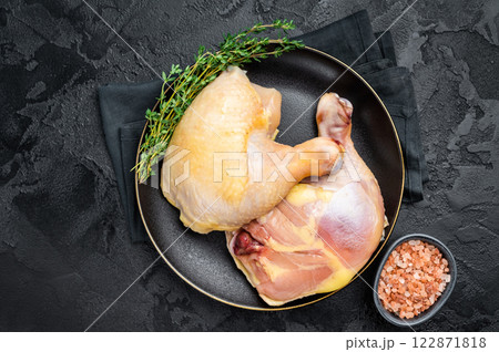 Chicken legs in a plate with herbs, farm poultry raw meat on black background, top view 122871818