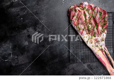 Whole raw Goat leg Marinated with herbs and olive oil. black background. top view Whole raw Goat leg Marinated with herbs and olive oil. black background. top view 122871868